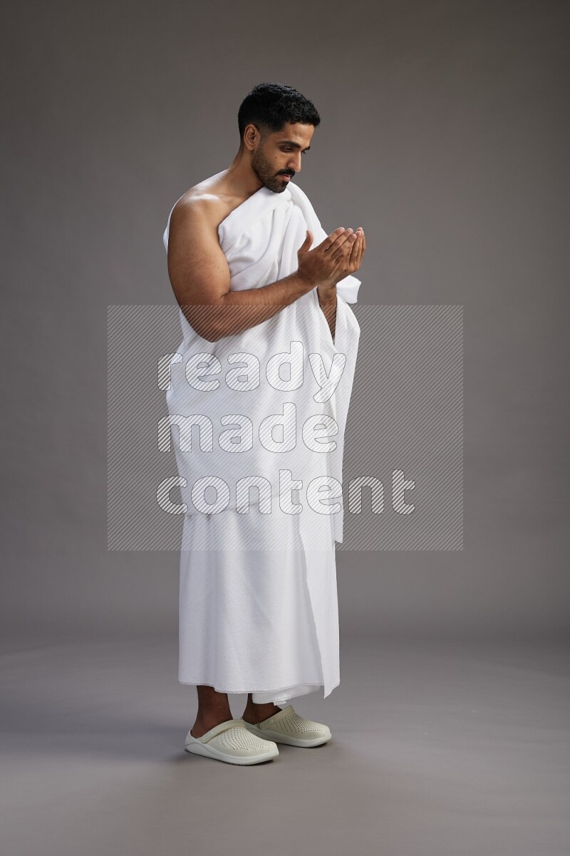 A man wearing Ehram Standing performing dua'a on gray background
