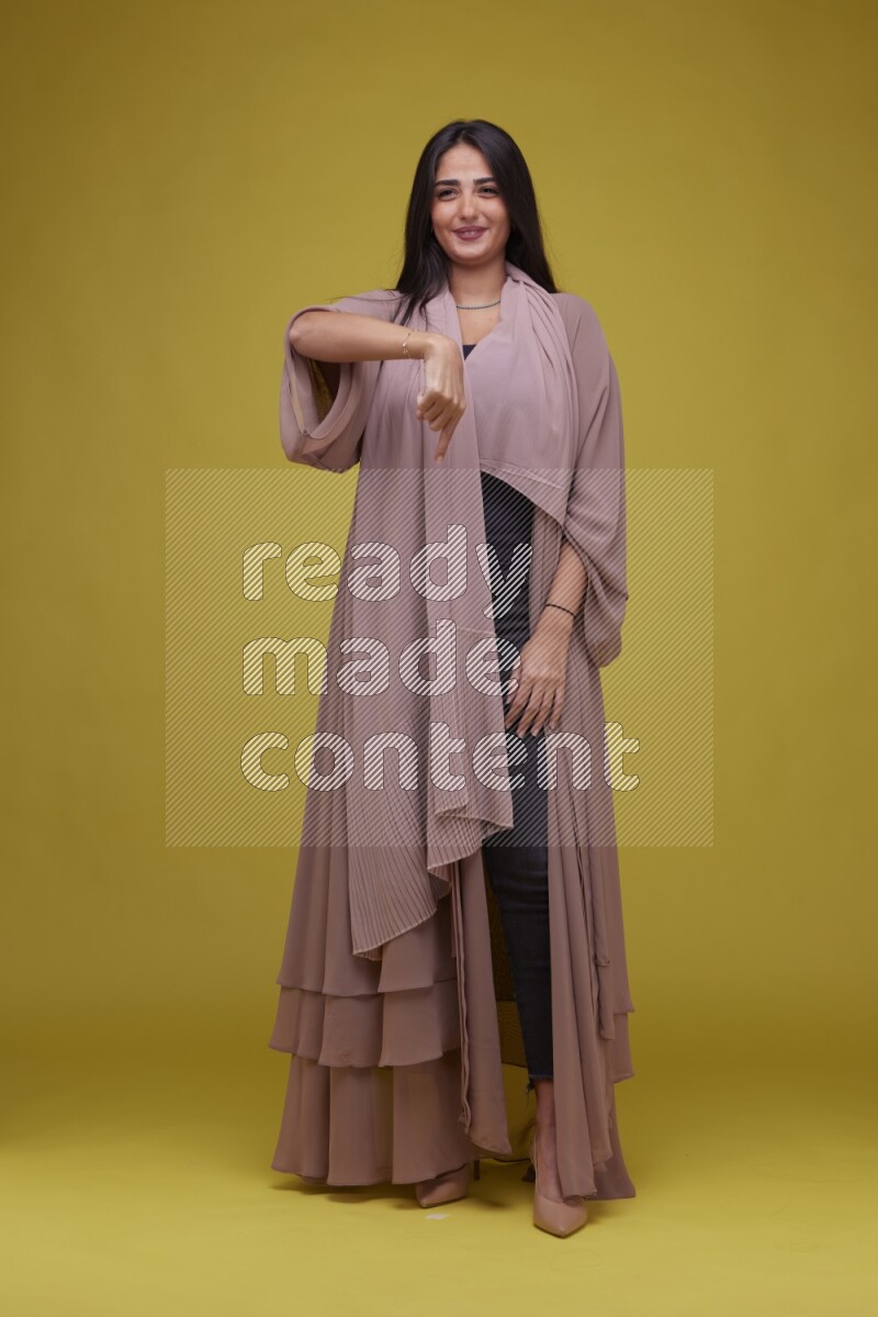 A woman Pointing on a Yellow Background wearing Brown Abaya
