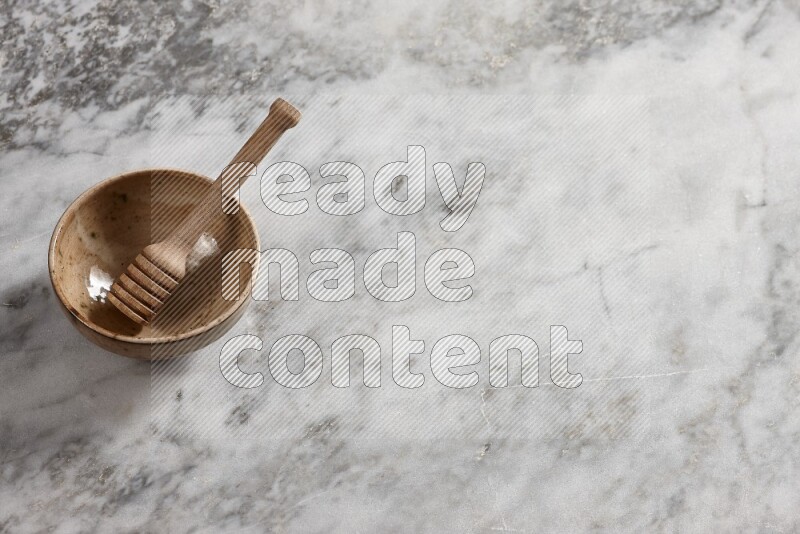 Beige pottery bowl with wooden honey dipper in it on grey marble background
