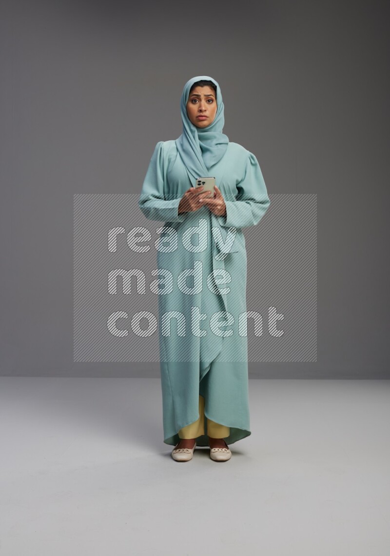 Saudi Woman wearing Abaya standing texting on phone on Gray background