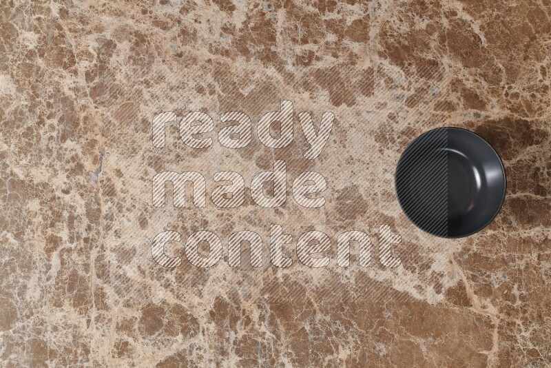 A black ceramic bowl on beige marble background