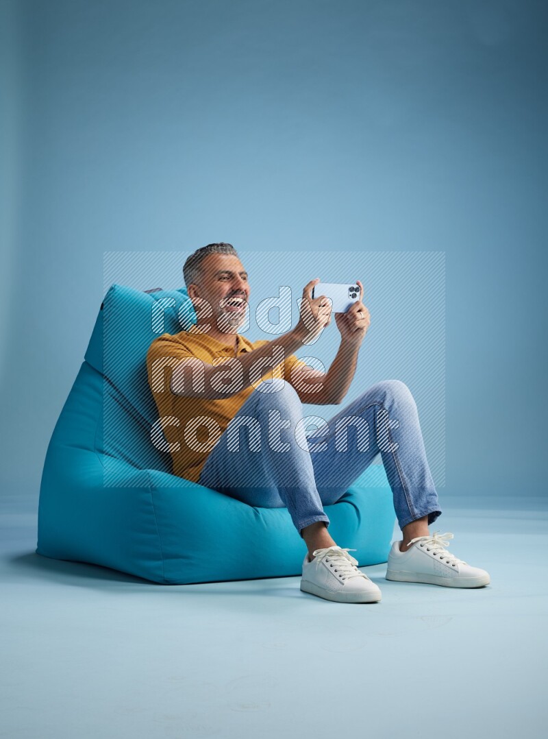 A man sitting on a blue beanbag and playing on phone