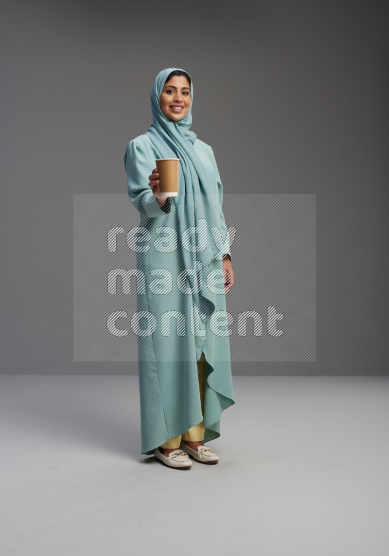 Saudi Woman wearing Abaya standing  holding paper cup on Gray background