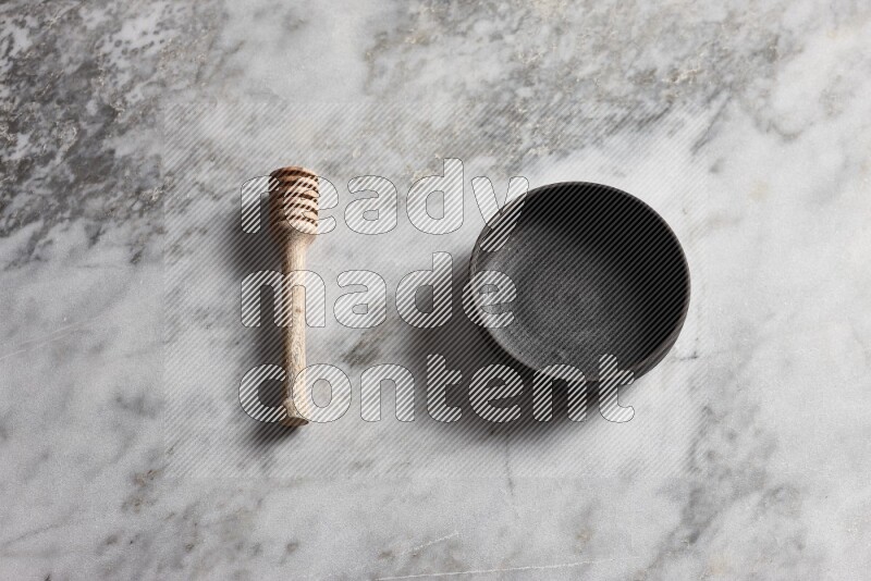 Black pottery bowl with wooden honey dipper on the side on grey marble background
