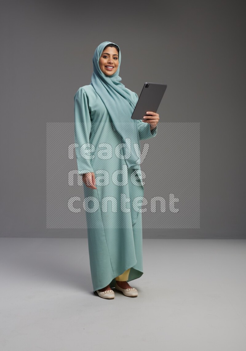 Saudi Woman wearing Abaya standing working on tablet on Gray background