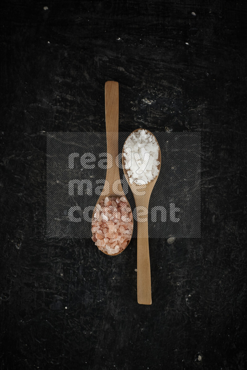 2 wooden spoons filled with fine and coarse salt on black background