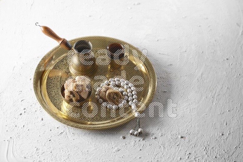 Dried figs in a metal bowl with coffee and prayer beads on a tray in a light setup