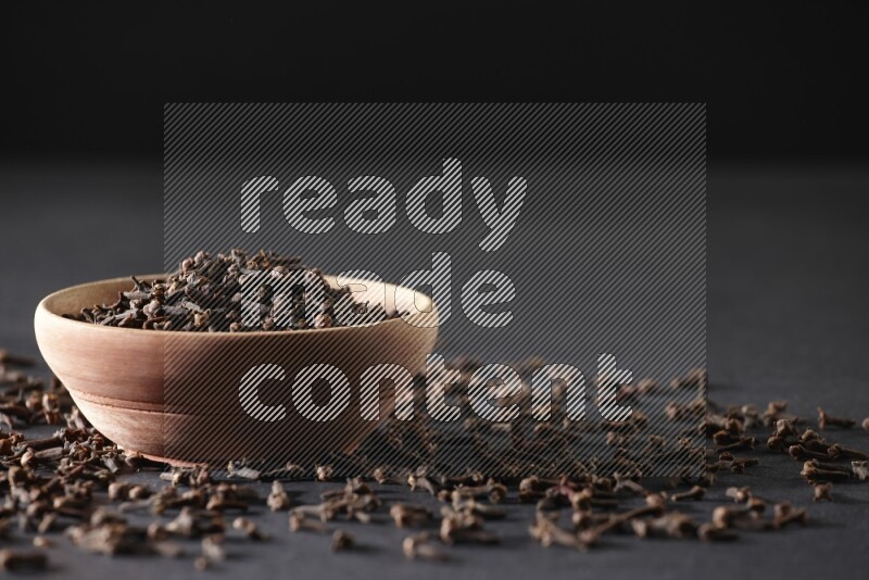 وعاء خشبي ممتلئ بحبوب القرنفل مع حبوب القرنفل المتناثرة على خلفية سوداء