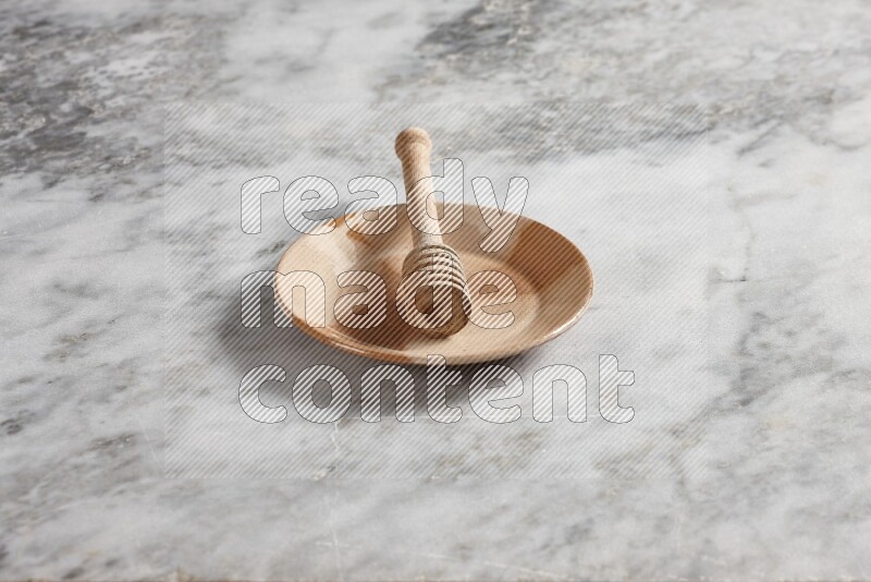 Multicolored pottery plate with wooden honey dipper in it on grey marble background