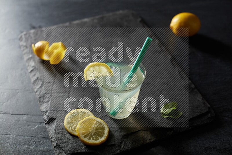 A glass of lemon juice with a straw on black background