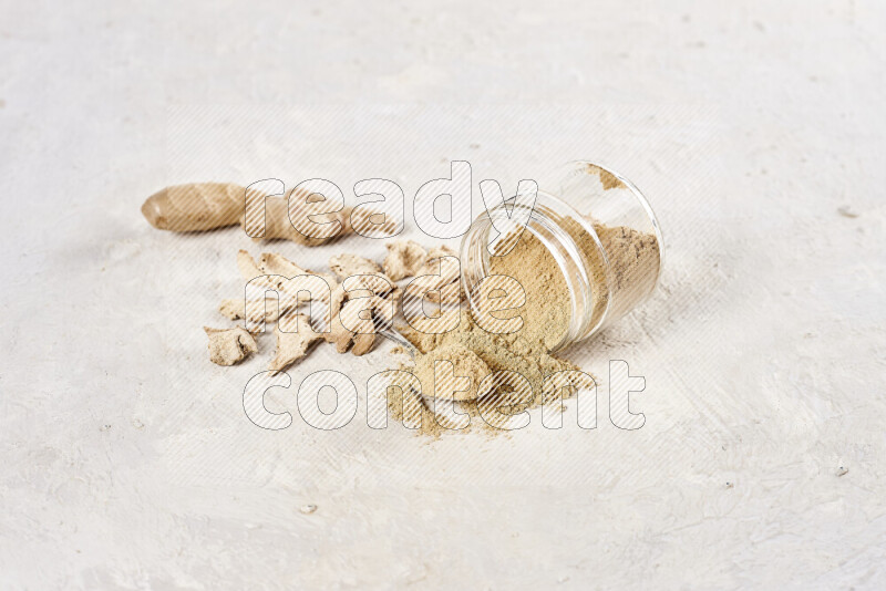 A glass jar full of ground ginger powder flipped with some spilling powder on white background