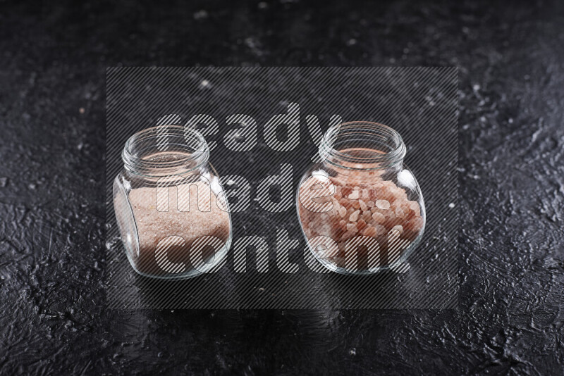 2 glass jars one is filled with fine himalayan salt and the other with coarse himalayan salt on black background