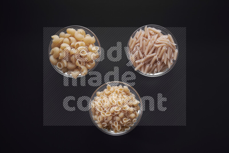 Different pasta types in glass bowls on black background