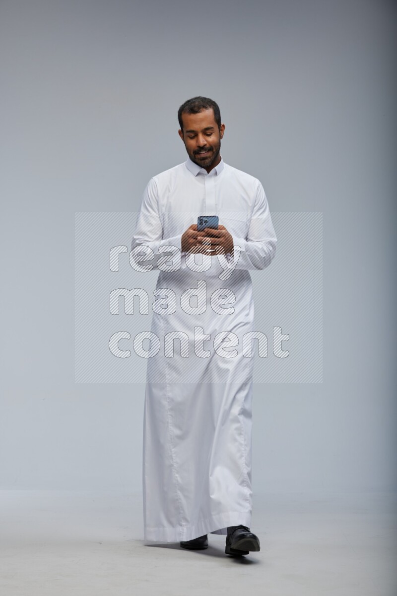 Saudi man wearing Thob standing texting on phone on Gray background