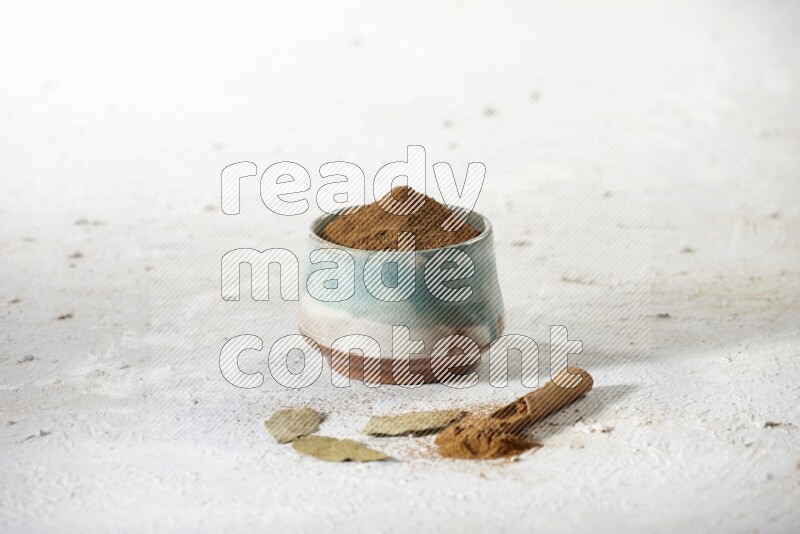 Cinnamon powder in a ceramic bowl with cinnamon sticks and laurel leaves on white background