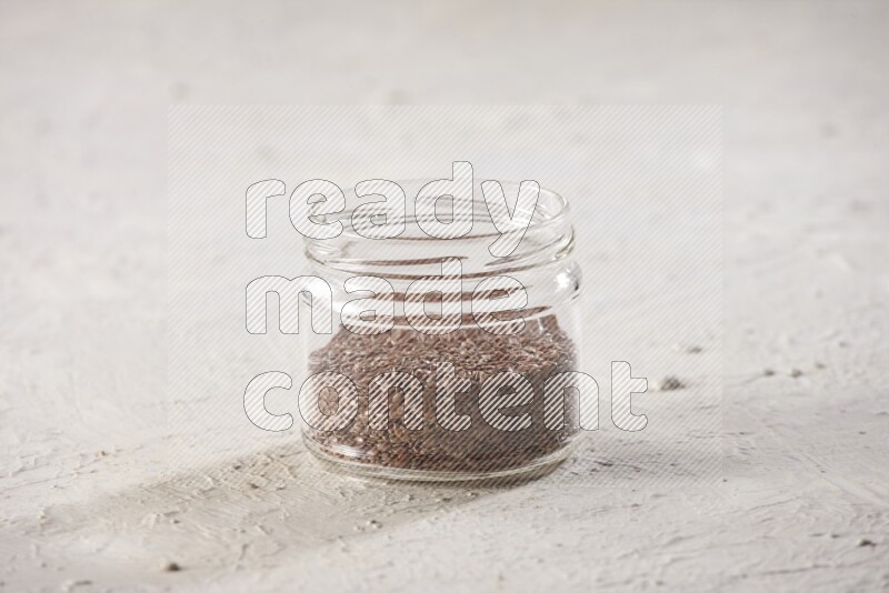 A glass jar full of flax seeds on a textured white flooring