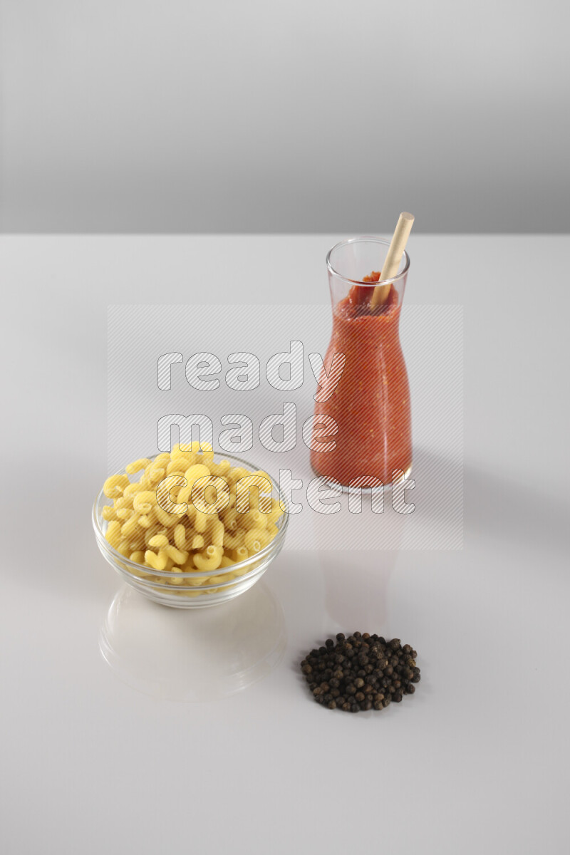 Raw pasta with tomatoe pasta with different ingredients such as cherry tomatoes, basil, garlic, bay laurel, cardamom, white pepper, black pepper, red chilis and wheat stalks on light grey background