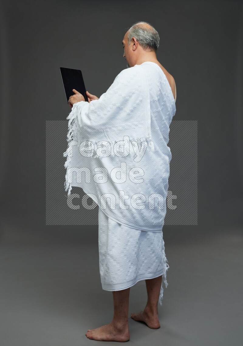 A man wearing Ehram Standing working on tablet on gray background
