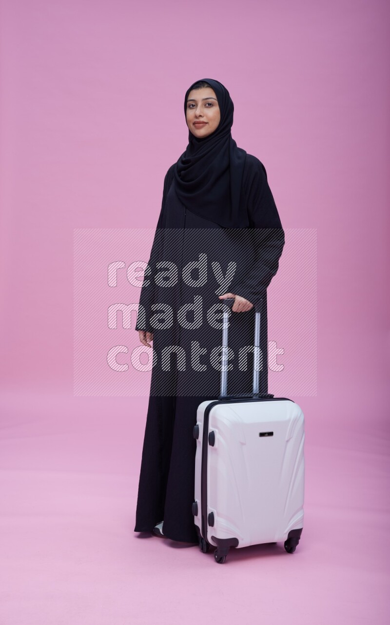 Saudi woman wearing Abaya standing holding bag on pink background