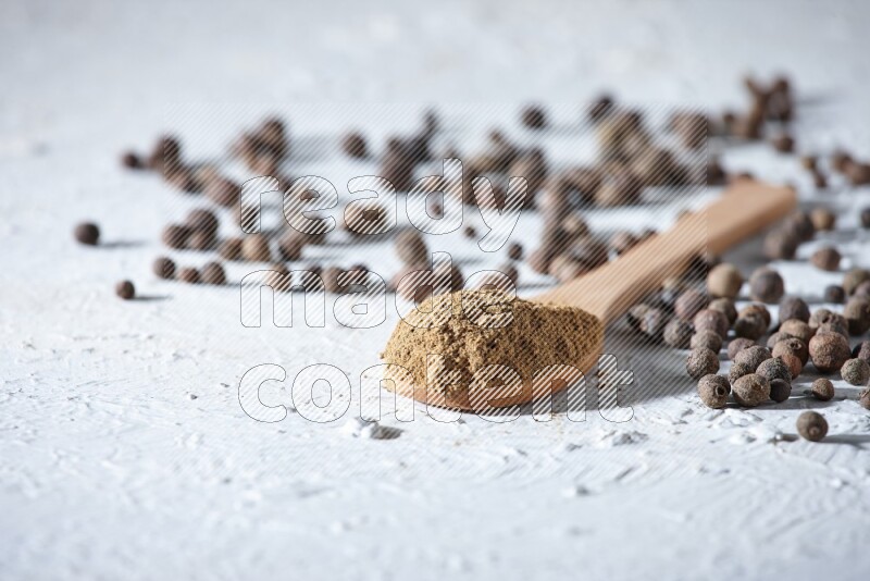 Wooden spoons full of allspice powder and allspice whole balls spreaded on a textured white flooring