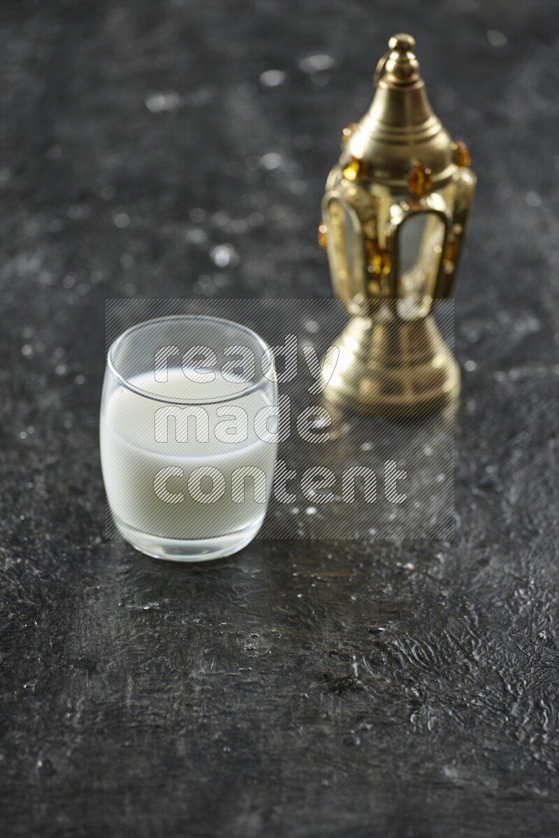 A golden lantern with different drinks, dates, nuts, prayer beads and quran on textured black background