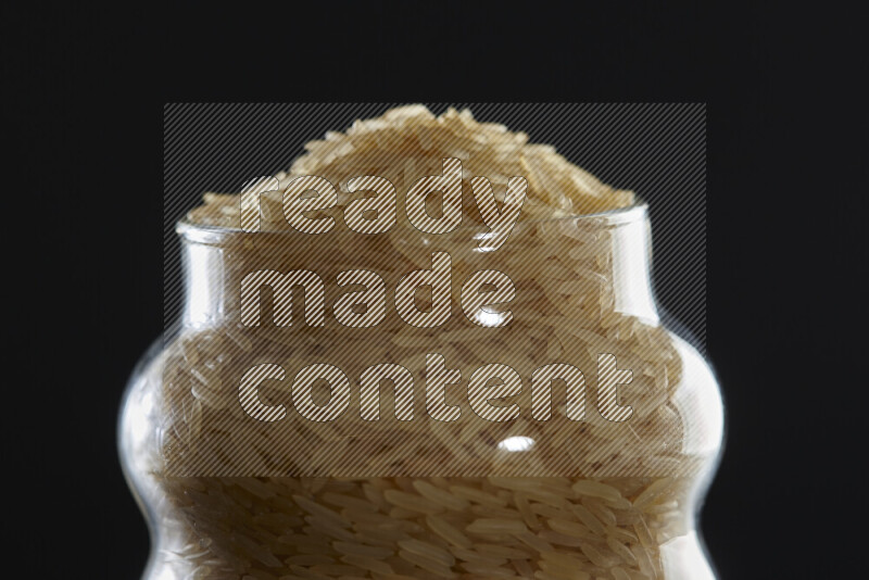 Basmati golden rice in a glass jar on black background