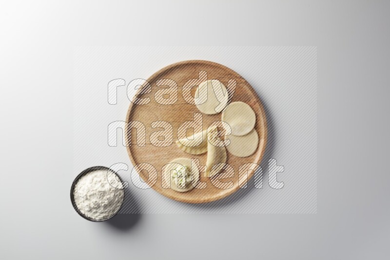 two closed sambosas and one open sambosa filled with cheese while flour aside in a wooden dish on a white background