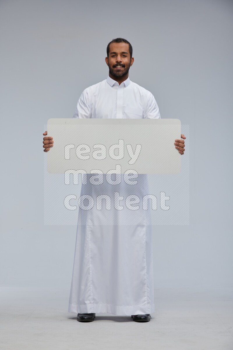 Saudi man wearing Thob standing holding board on Gray background