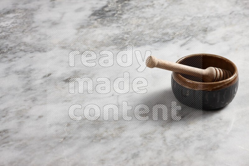 Multicolored pottery bowl with wooden honey dipper in it on grey marble background