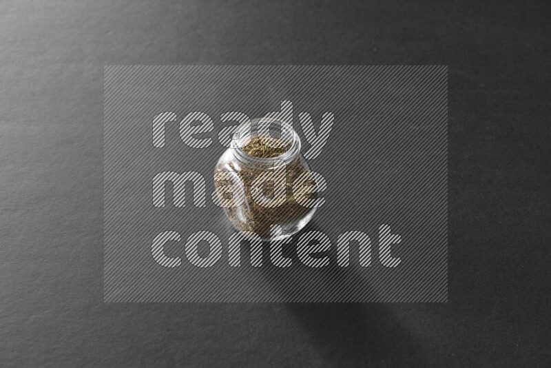 A glass spice jar full of cumin on black flooring