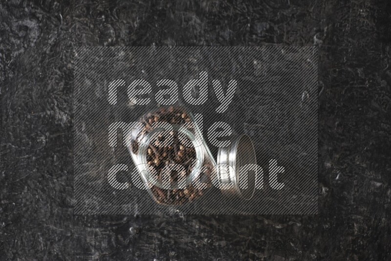 A glass spice jar full of cloves on textured black flooring