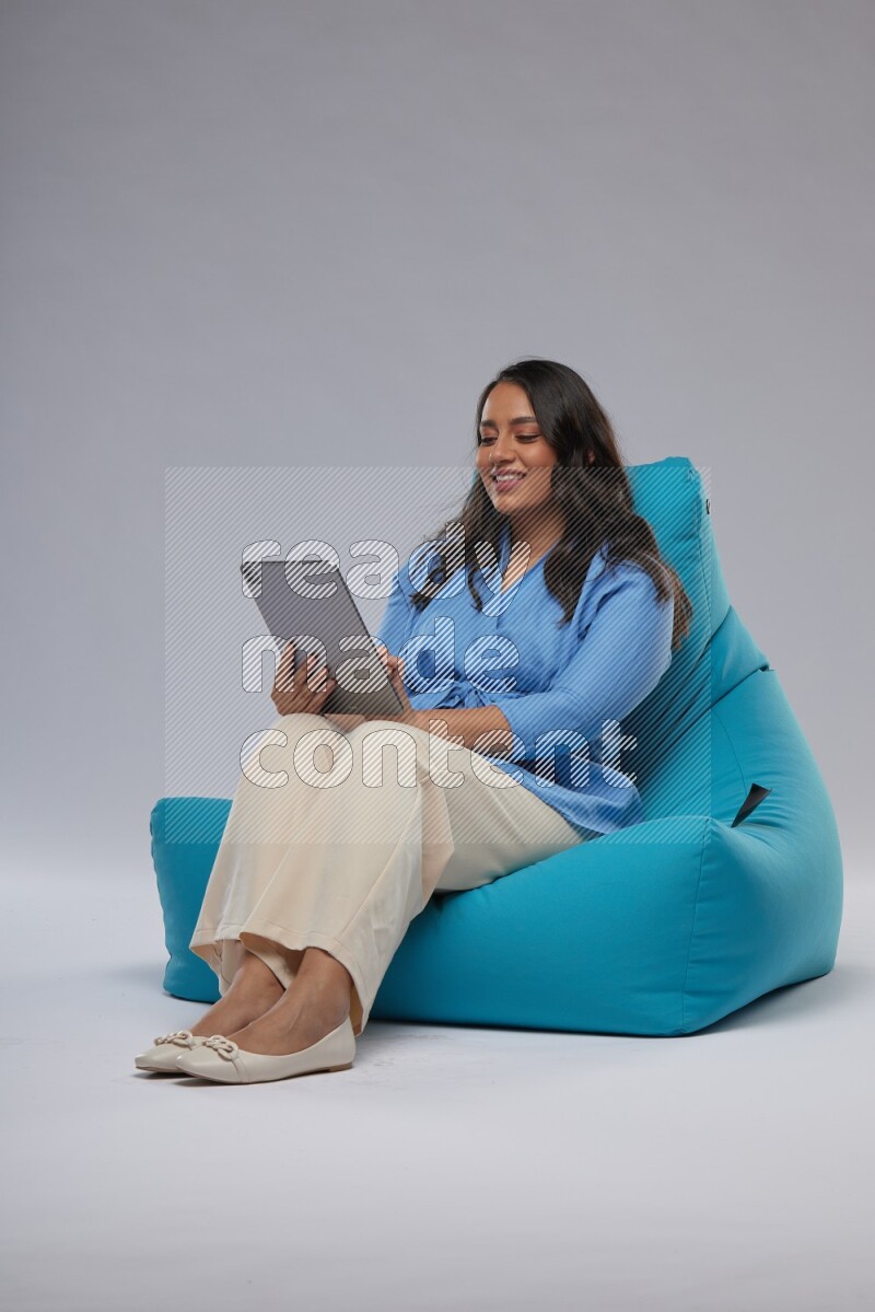 A woman sitting on a blue beanbag and working on tablet
