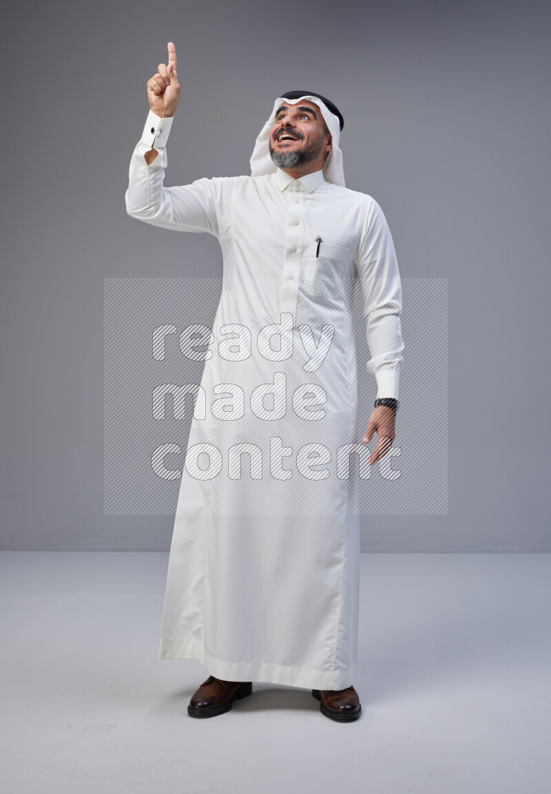 Saudi man Wearing Thob and white Shomag standing interacting with the camera on Gray background