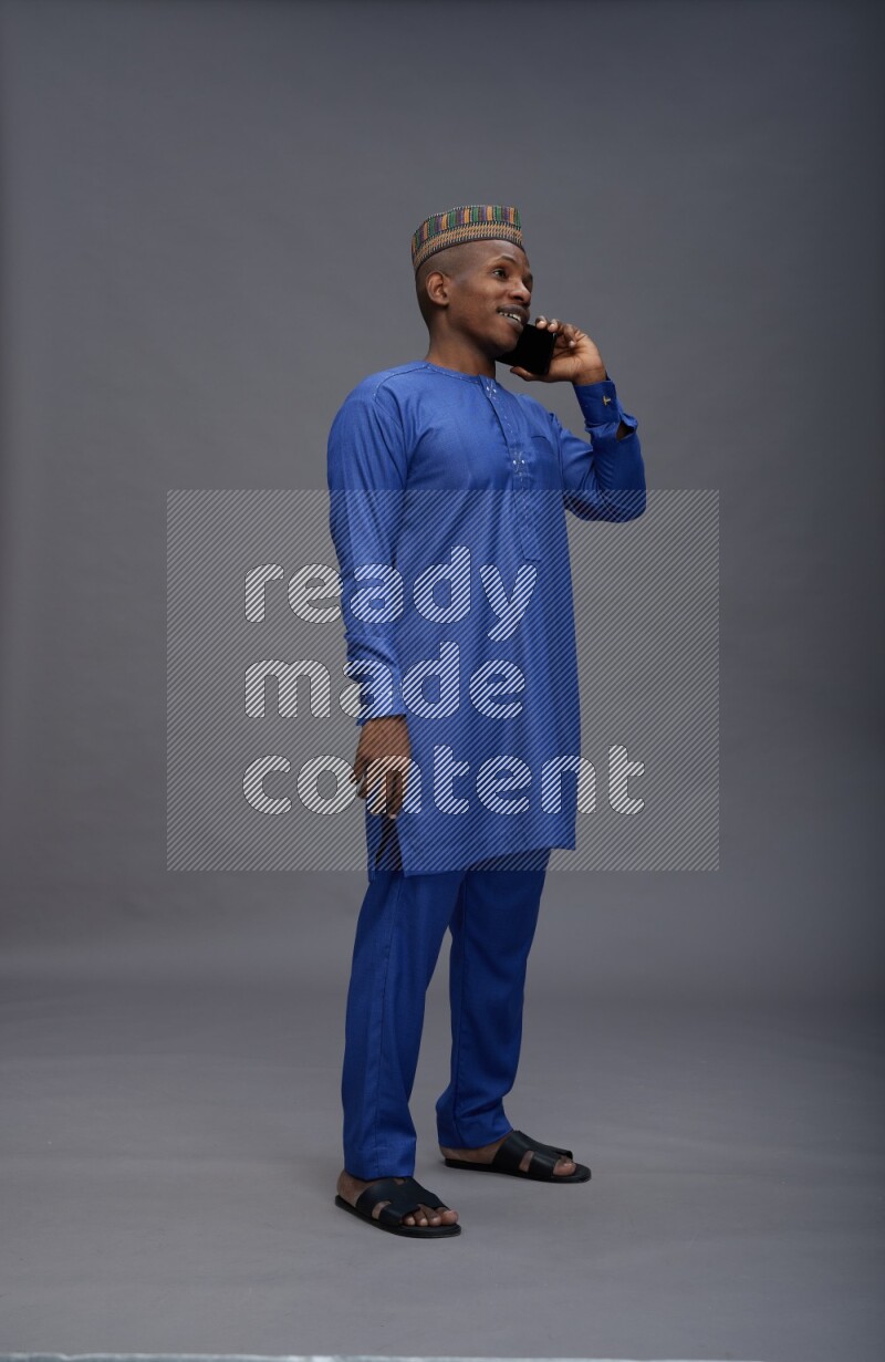 Man wearing Nigerian outfit standing talking on phone on gray background