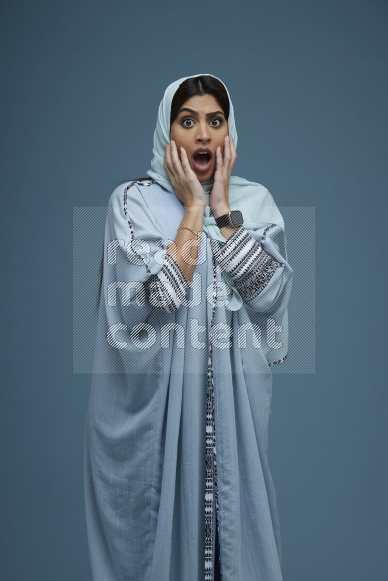 A woman posing in a blue background wearing a blue Abaya with hijab