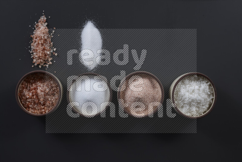 4 pottery bowls filled with himalayan salt and white salt on black background