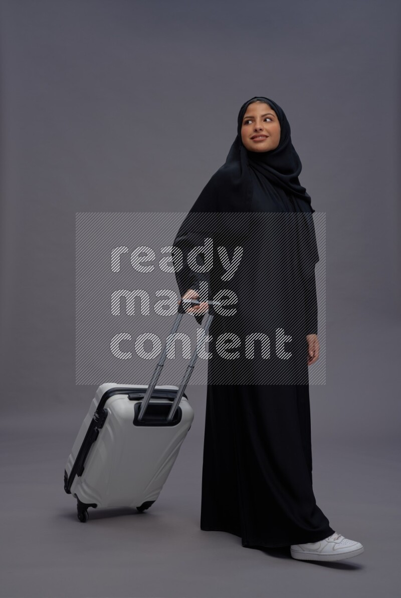 Saudi woman wearing Abaya standing holding bag on gray background