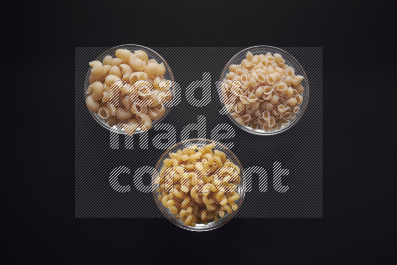 Different pasta types in glass bowls on black background