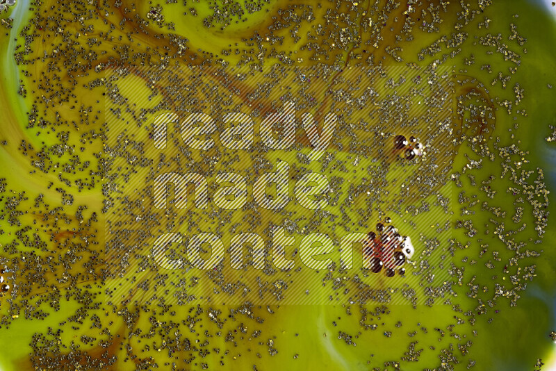 A close-up of sparkling gold glitter scattered on swirling green and red background
