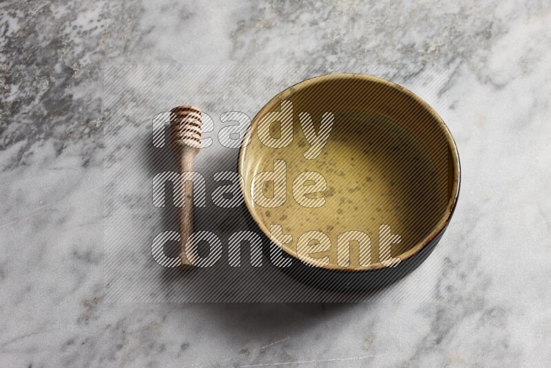 Multicolored pottery oven plate with wooden honey dipper on the side on grey marble background