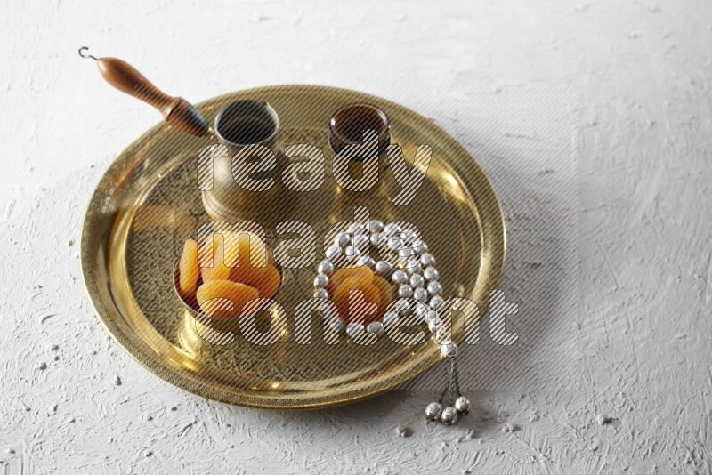 Dried apricots in a metal bowl with coffee and prayer beads on a tray in a light setup