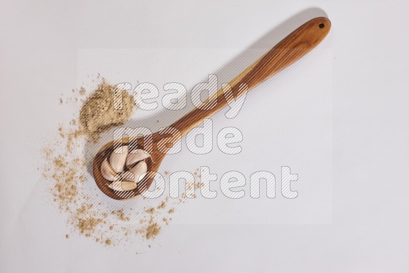 A wooden ladle full of garlic cloves with sprinkled powder on a white flooring