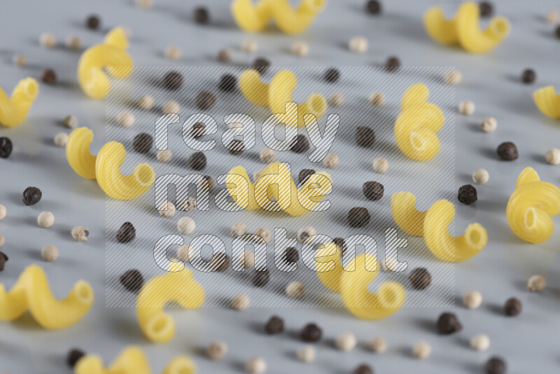 Raw pasta with different ingredients such as cherry tomatoes, garlic, onions, red chilis, black pepper, white pepper, bay laurel leaves, rosemary, cardamom and mushrooms on light blue background