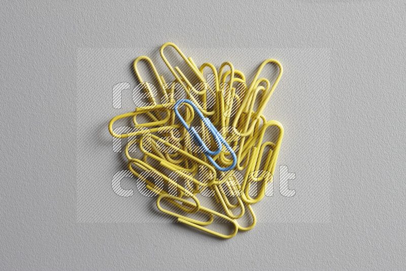 A bunch of yellow paper clips with a different colored paper clip in the center on grey background