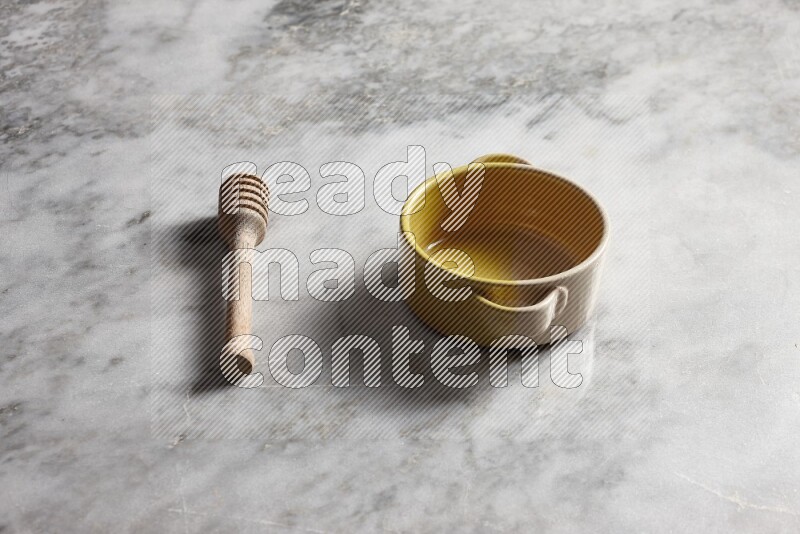 Multicolored pottery bowl with wooden honey dipper on the side on grey marble background