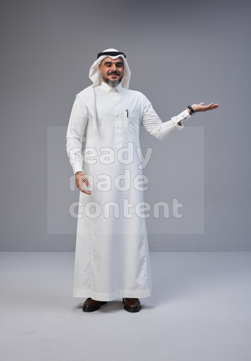 Saudi man Wearing Thob and white Shomag standing interacting with the camera on Gray background