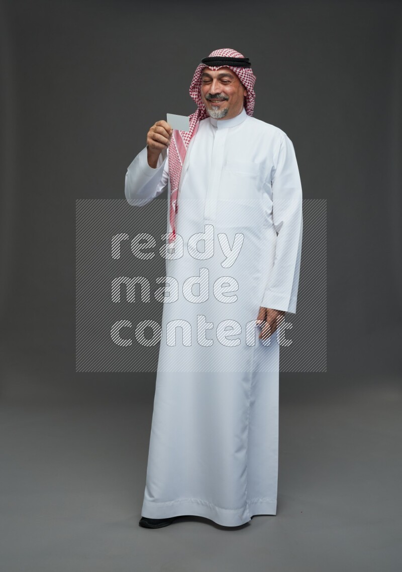 Saudi man with shomag Standing holding ATM card on gray background