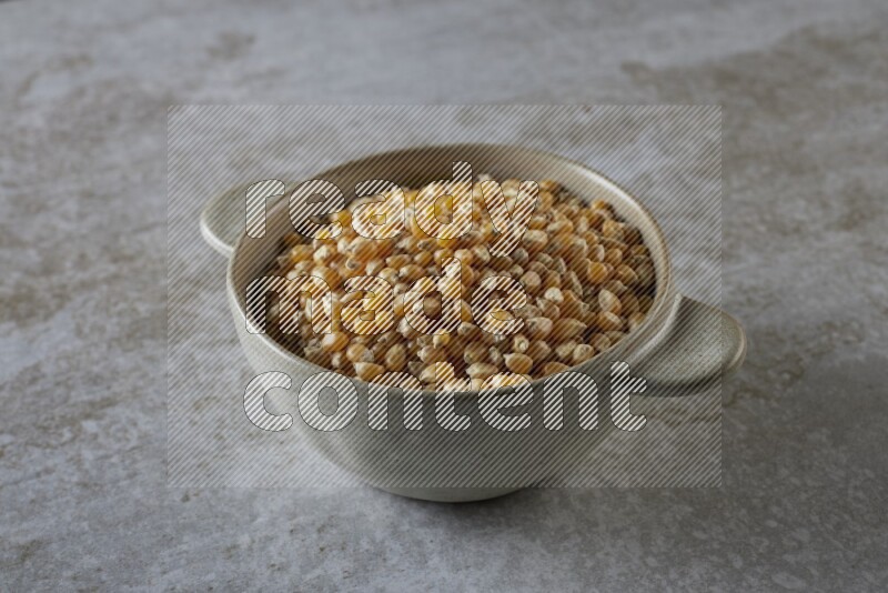 corn kernel in a off-white handheld ceramic bowl on a grey textured countertop