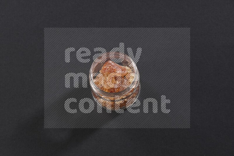 A glass jar full of gum arabic on black flooring