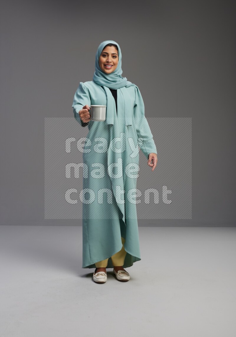 Saudi Woman wearing Abaya standing  holding a mug on Gray background